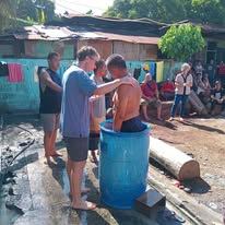 Two men beside a blue water barrel during a gathering